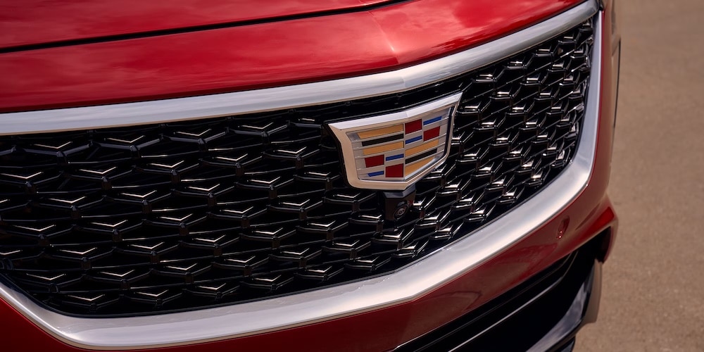Close-up of a red car's front grille featuring a prominent Cadillac logo.