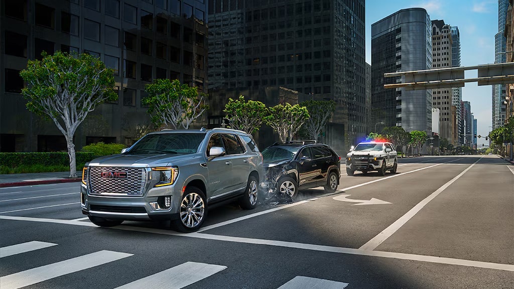SUVs and a police car involved in a minor collision on a city street lined with trees and skyscrapers.