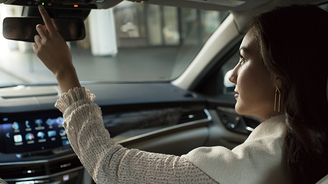 Woman adjusting the rearview mirror inside a modern car with a digital dashboard.