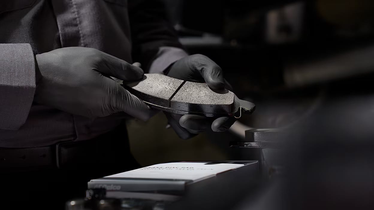 Mechanic wearing gloves holds car brake pads in a workshop setting.