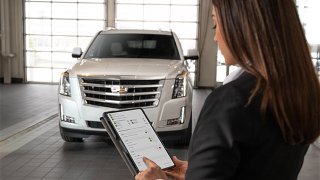 A woman uses a tablet to assess a white SUV in a garage.
