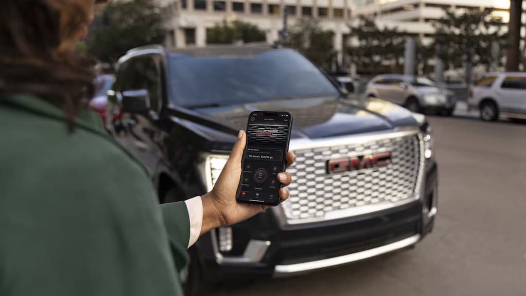 Person using a smartphone app to control a GMC vehicle parked on the street.